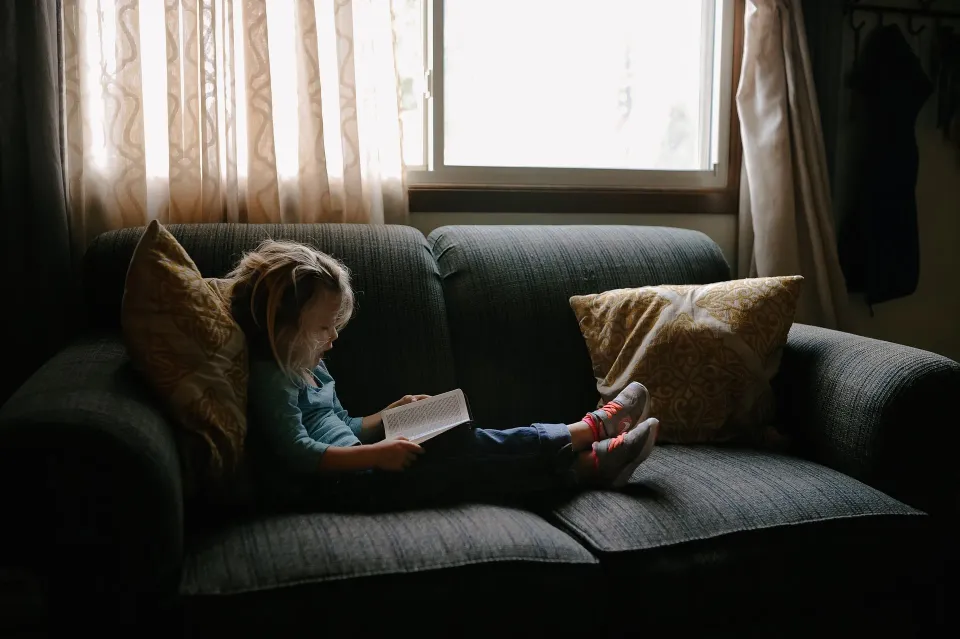Niña leyendo en un sofá.
